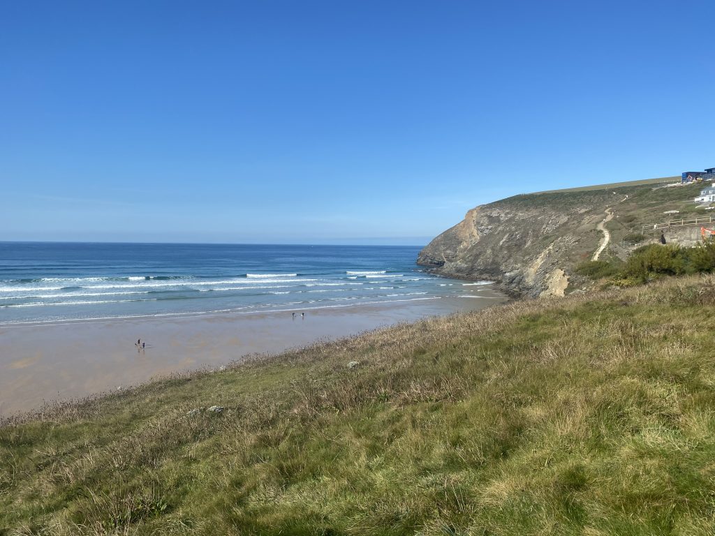 Mawgan Porth Beach in Cornwall with sandy shoreline, rolling waves and dramatic coastal cliffs