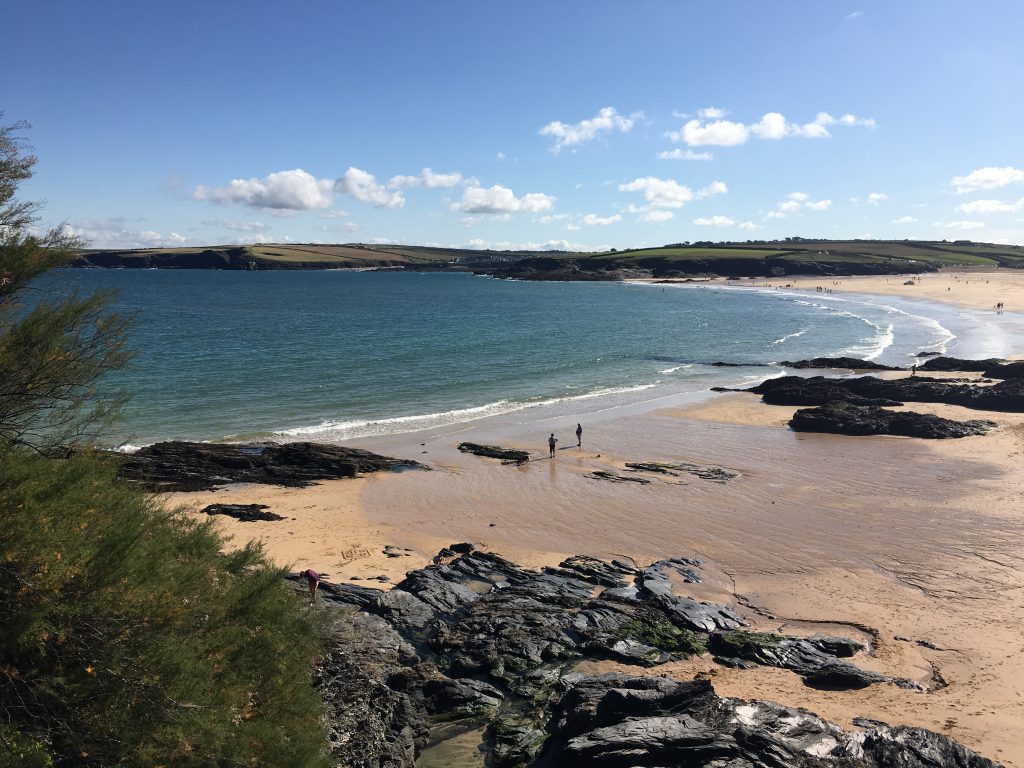Harlyn Bay beach in Cornwall with golden sand, gentle waves and rocky shoreline on a clear day.