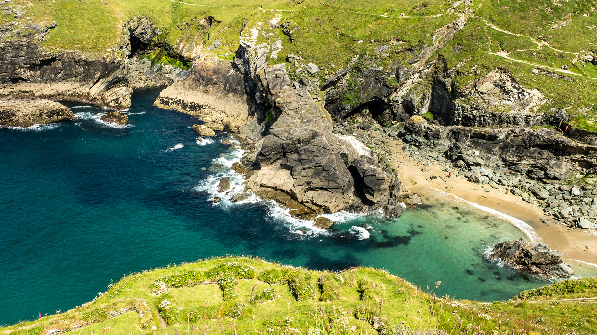 Aerial view of Tintagel Haven (Castle Cove) in North Cornwall, showing turquoise sea, rugged cliffs and a small sandy beach below