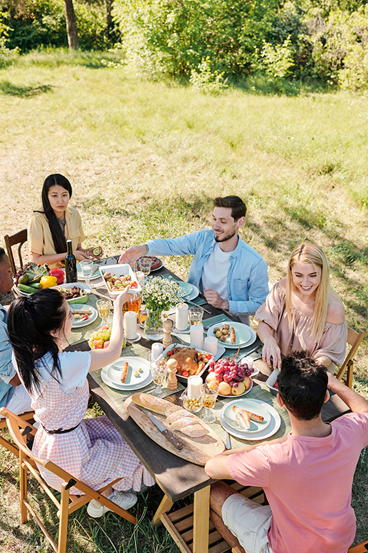 Friends enjoying a relaxed outdoor meal together around a table in a garden setting.